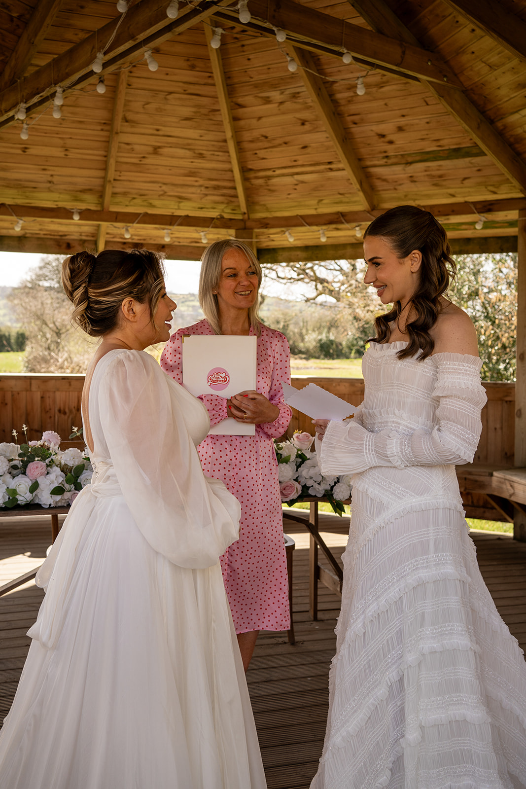 Gill, inclusive wedding celebrant in Lancashire and the North West, officiating a same-sex wedding outdoors at a pergola with two brides